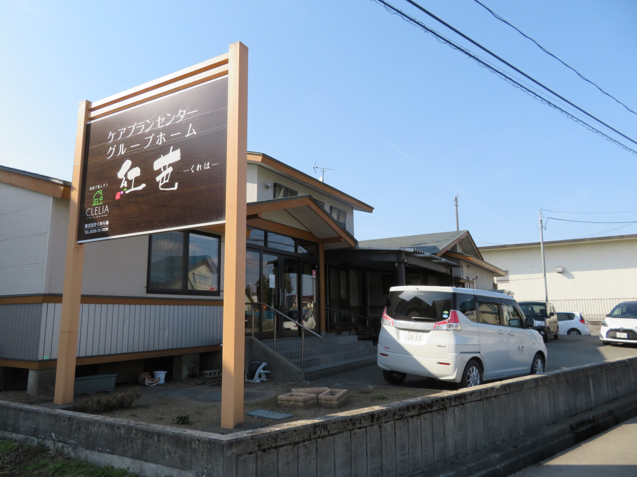 介護施設の建物外観と駐車場。木製の大きな看板が目印。